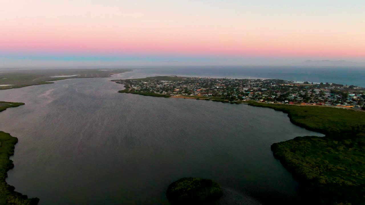 Aerial lagoon view with town along the shoreline under a pink evening sky.