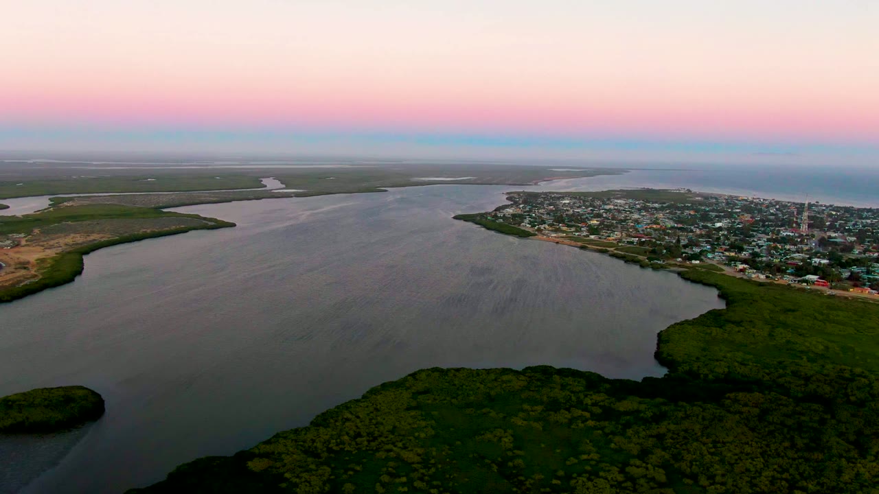 Wide aerial river view with a town on the right and dense greenery in the foreground.