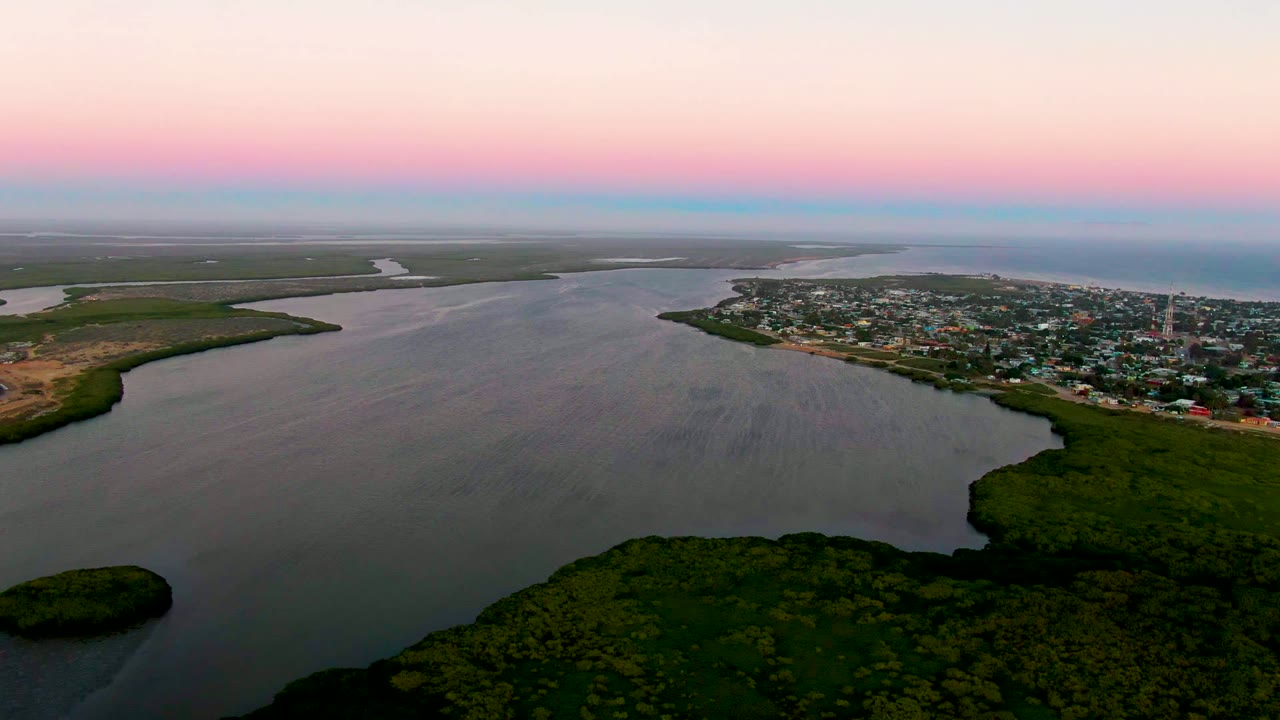 A high aerial view over San Carlos, Baja California Sur shows the waterway curving past marshland, the town clustered near the right shoreline, and no visible people.