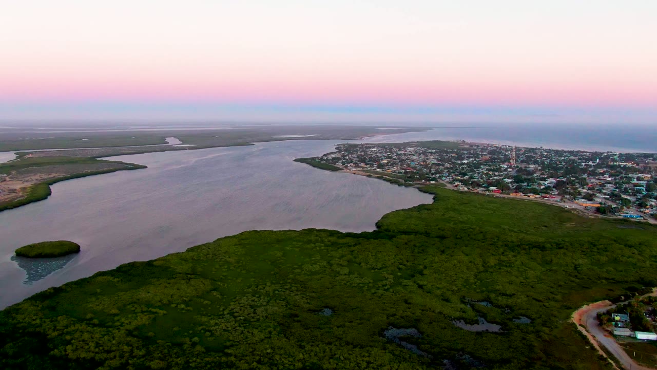 High aerial view across inlet water with green foreground vegetation and a small shoreline settlement.
