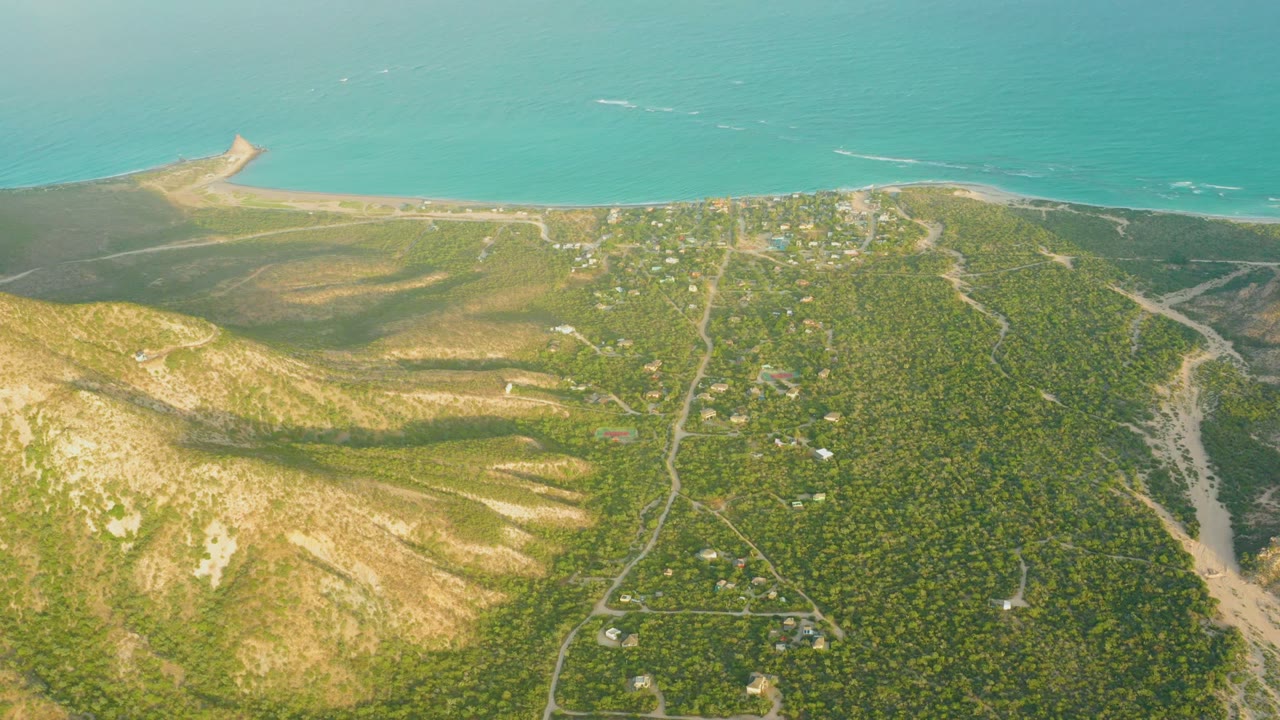 Aerial coastline view with sandy hillside, roads, beach, and blue-green water.