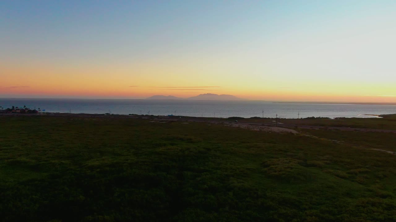 Dark grassy plain leading toward the ocean at sunset.