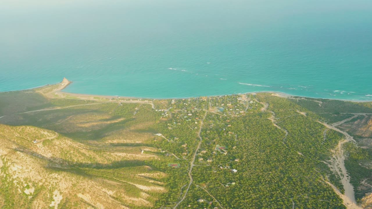 Drone view over green coastal terrain leading to a beach and sea.