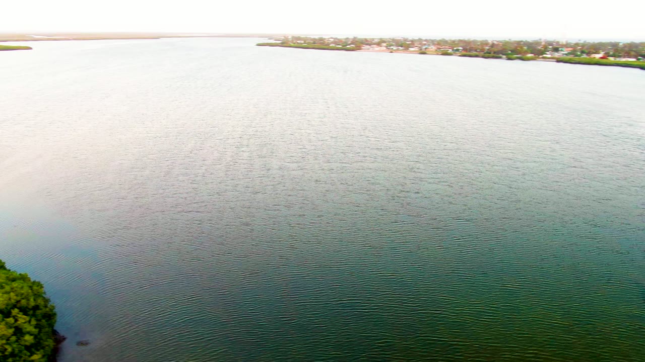 Aerial frame from San Carlos, Baja California Sur looking over rippled green-blue water toward a low distant shore with buildings and no visible people.