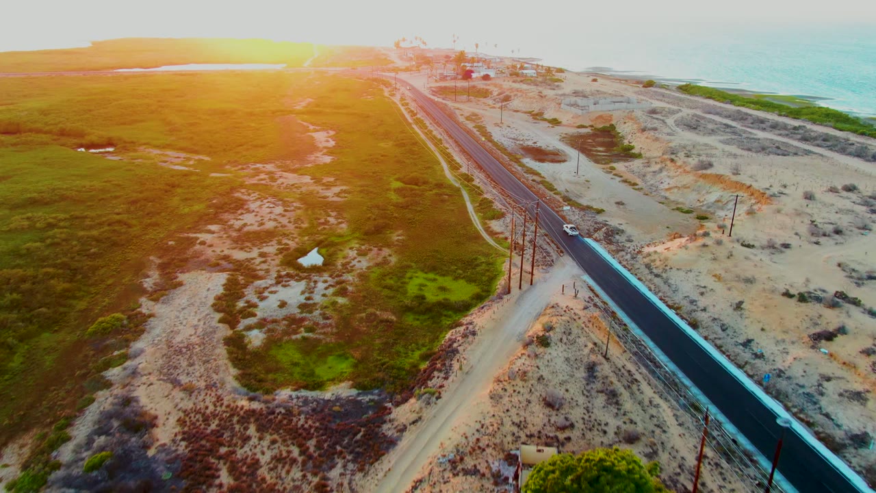 Car on a coastal road with dunes, grassland, and ocean in the distance.