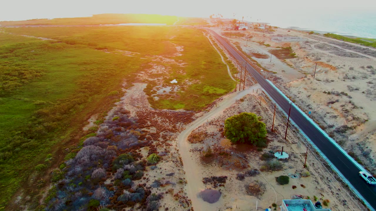 White car enters the lower right of a coastal road seen from above.