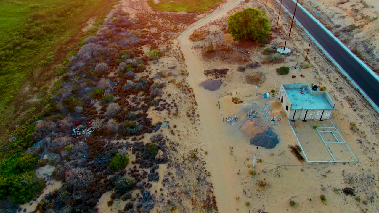 Oblique drone view of desert scrub, dirt tracks, a paved road, and a small building.
