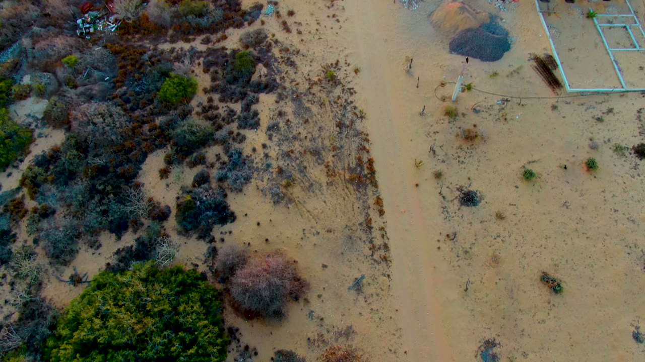 High overhead frame of sandy scrubland and a partially visible construction area in San Carlos, Baja California Sur, with no visible people.