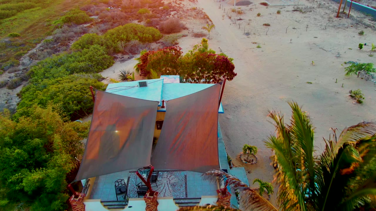 Drone view of fabric canopy over a small structure in sandy scrub.