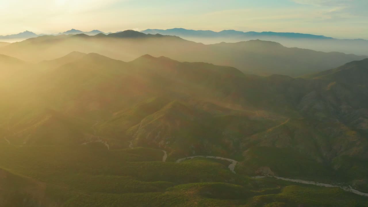 Layered ridges and a winding valley route under warm morning haze.