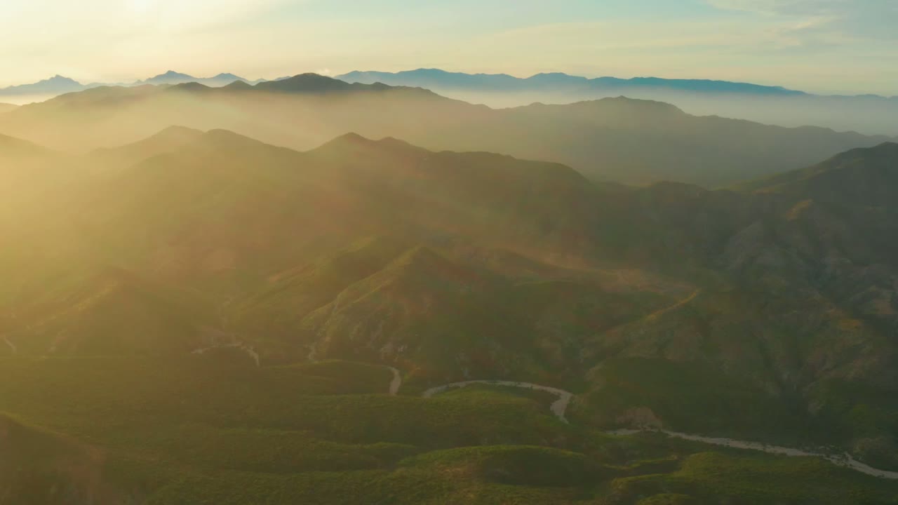 Cabo Pulmo aerial landscape with sunbeams washing the left hills, darker ridges to the right, distant mountains in haze, and no visible people.