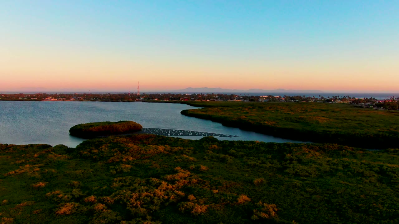 Curving inlet water with marsh grass and a low settlement in the distance.