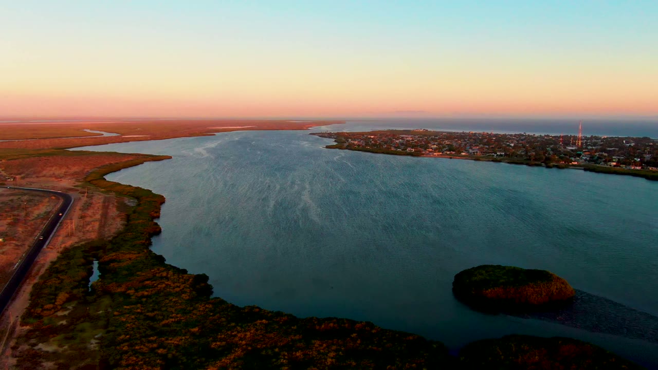 Aerial sunset view over river water, marshland, small island, and town shoreline.