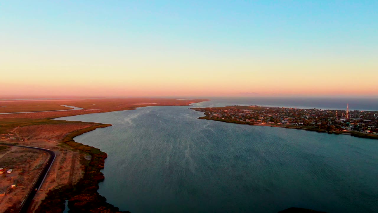 Wide sunset view across calm estuary water toward a town and distant horizon.