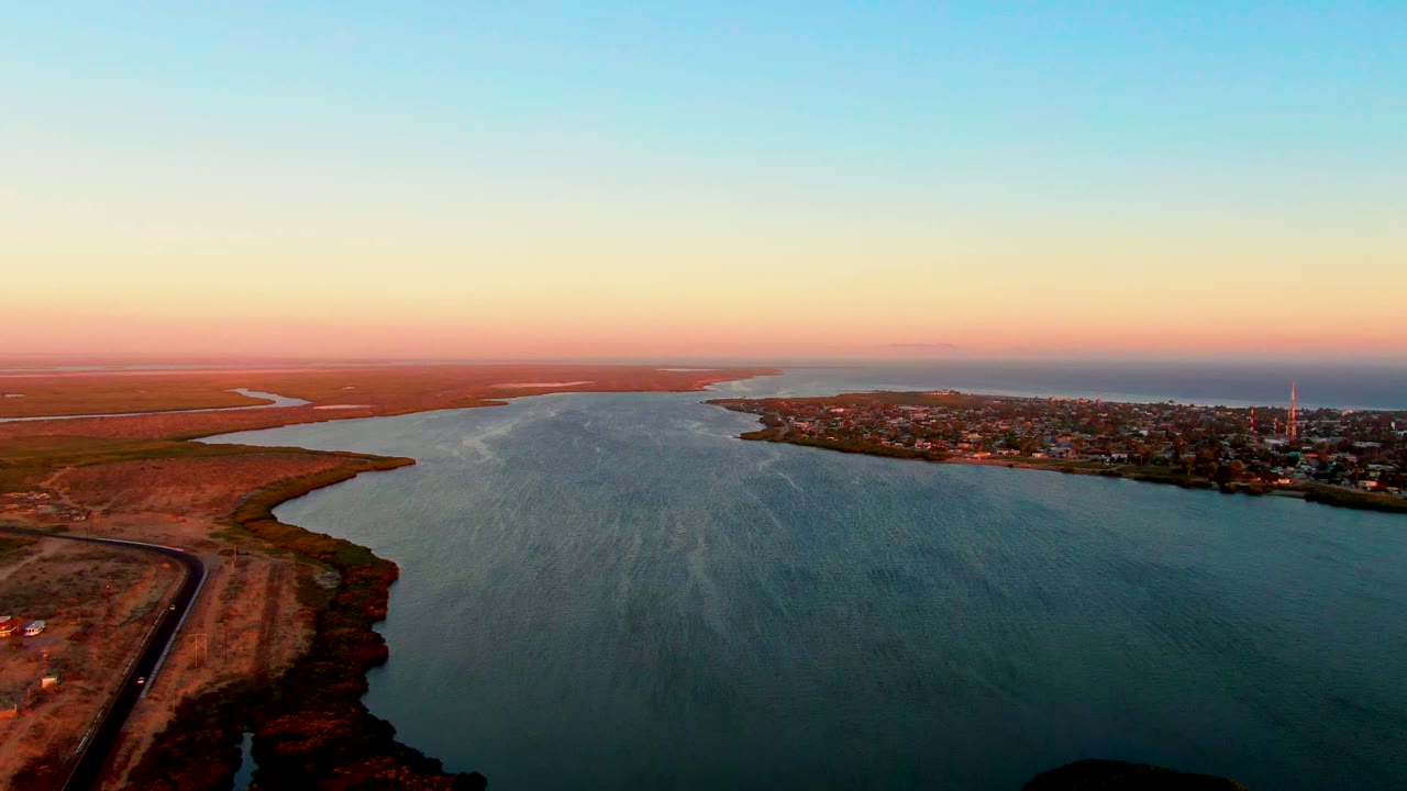 Two seconds into the San Carlos clip, the estuary remains centered with the town stretching along the right bank, open dry flats to the left, and no visible people.