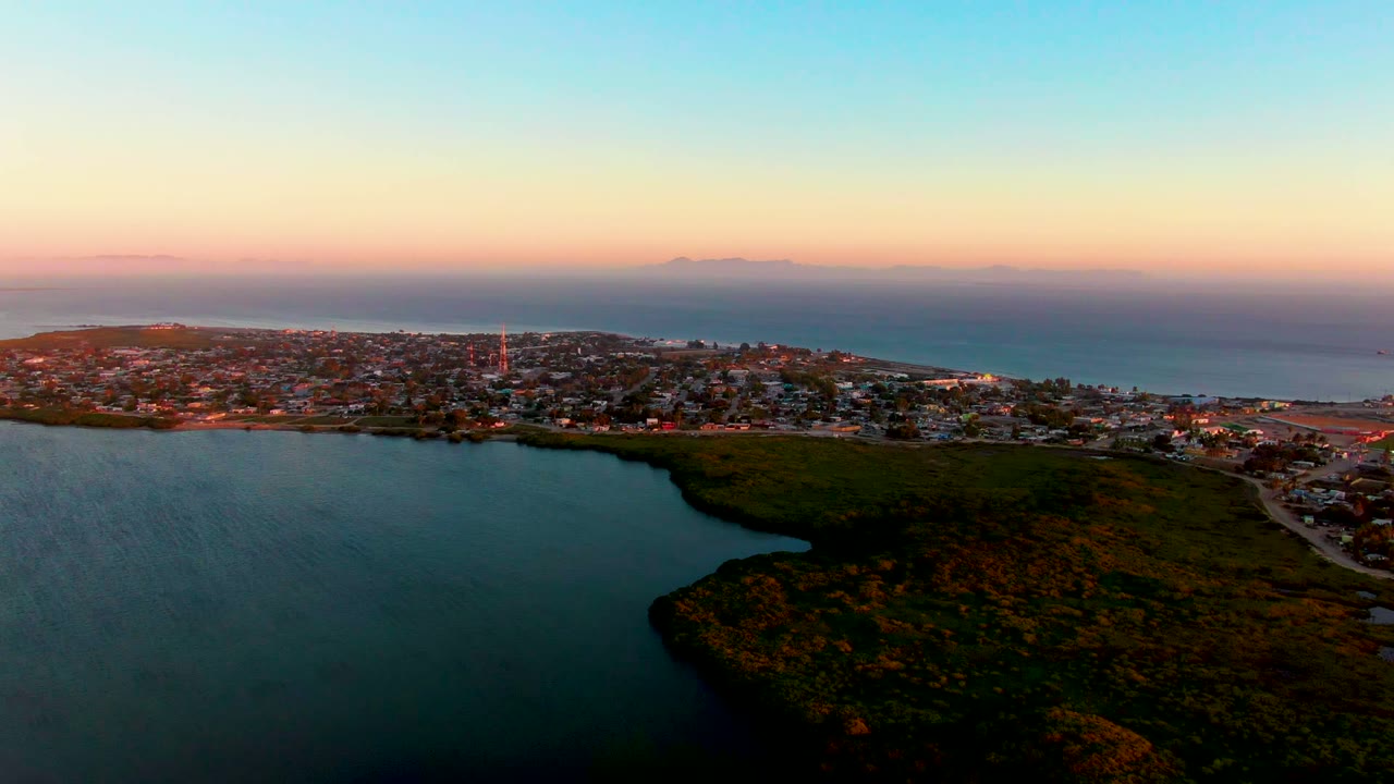 San Carlos, Baja California Sur appears beyond the lagoon and hill, with a pink band near the ocean horizon, darker water in the foreground, and no visible people.
