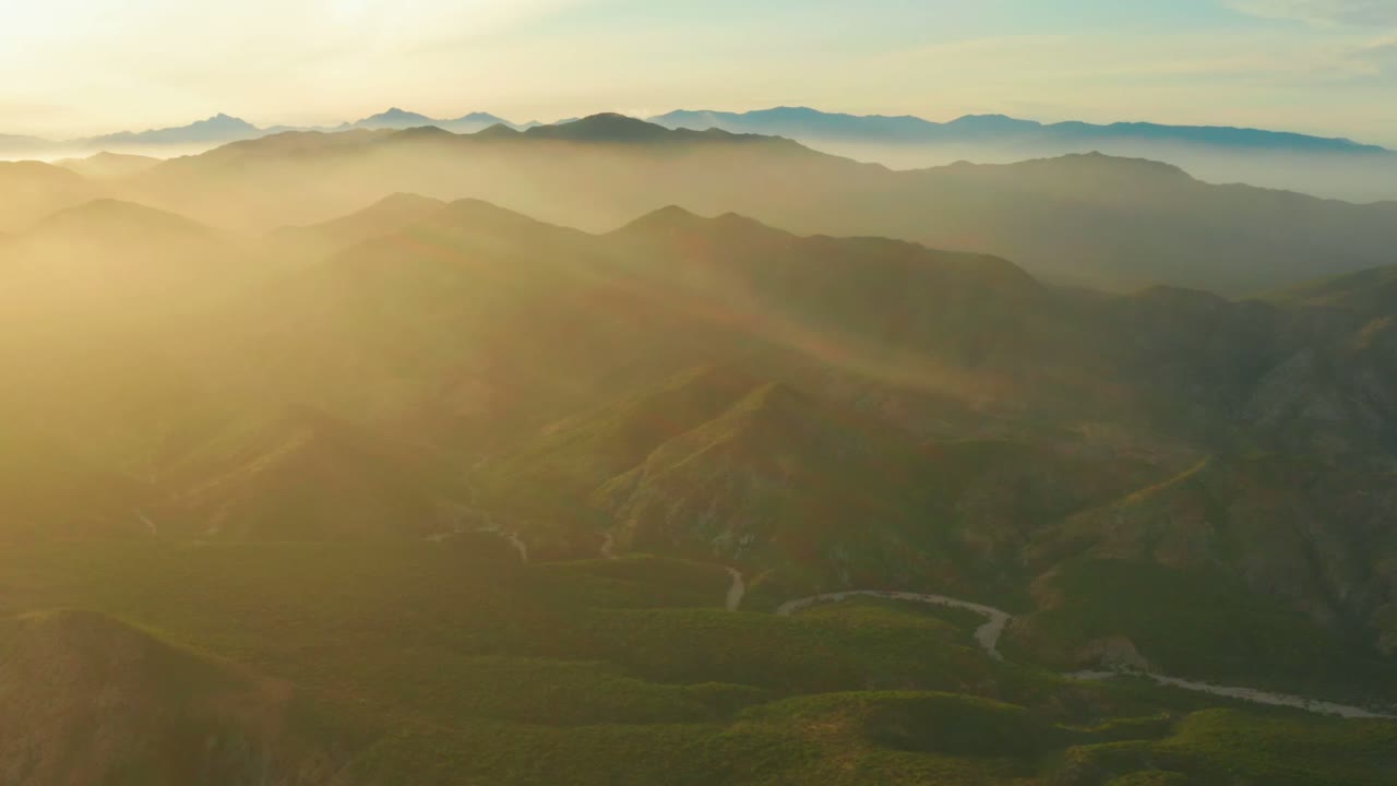 Sunlit mountain ridges with haze and a pale road in the valley.
