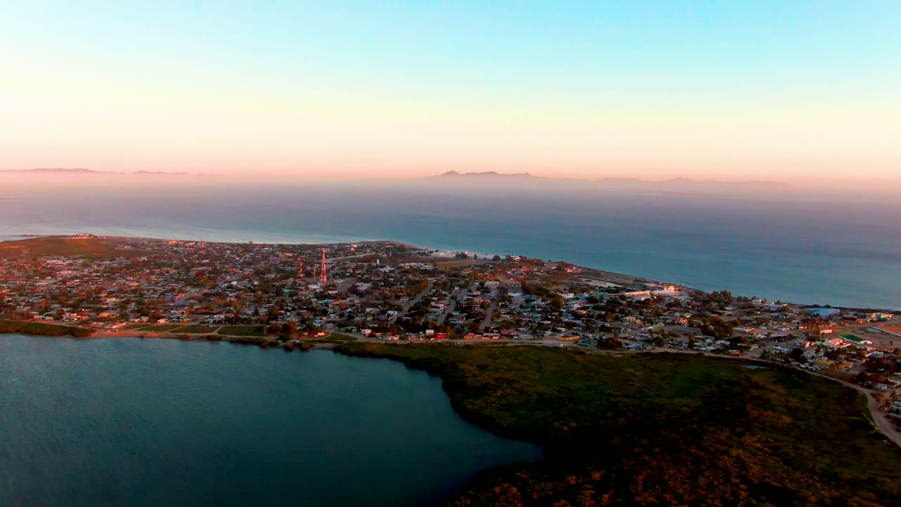 Wide coastal town view with lagoon foreground and pink-blue dusk sky.