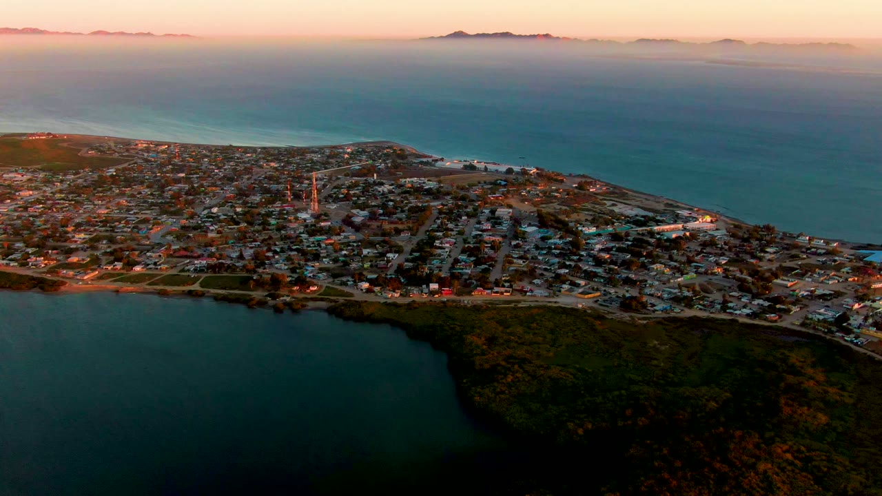 Coastal town blocks and shoreline under a pink evening sky.