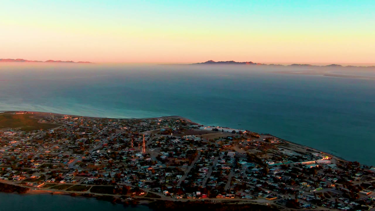 Coastal town and shoreline seen from above under a pink and blue sky.