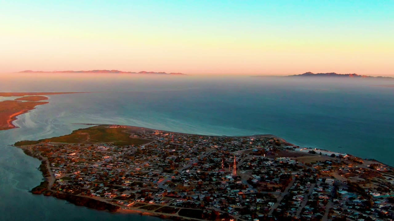 Coastal town and bay seen from above under a pink-blue sky.