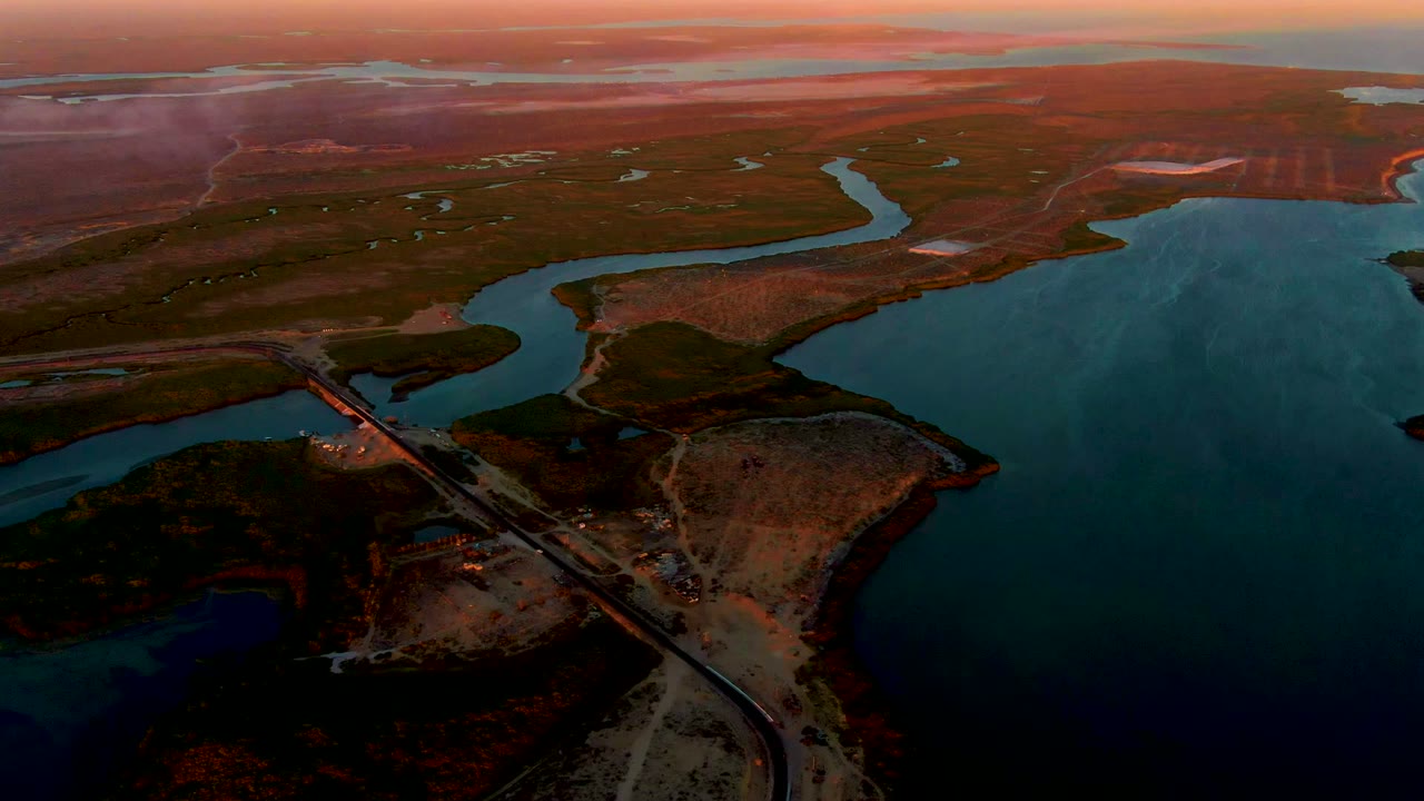 Dimming aerial view of water channel, bridge, and open terrain.