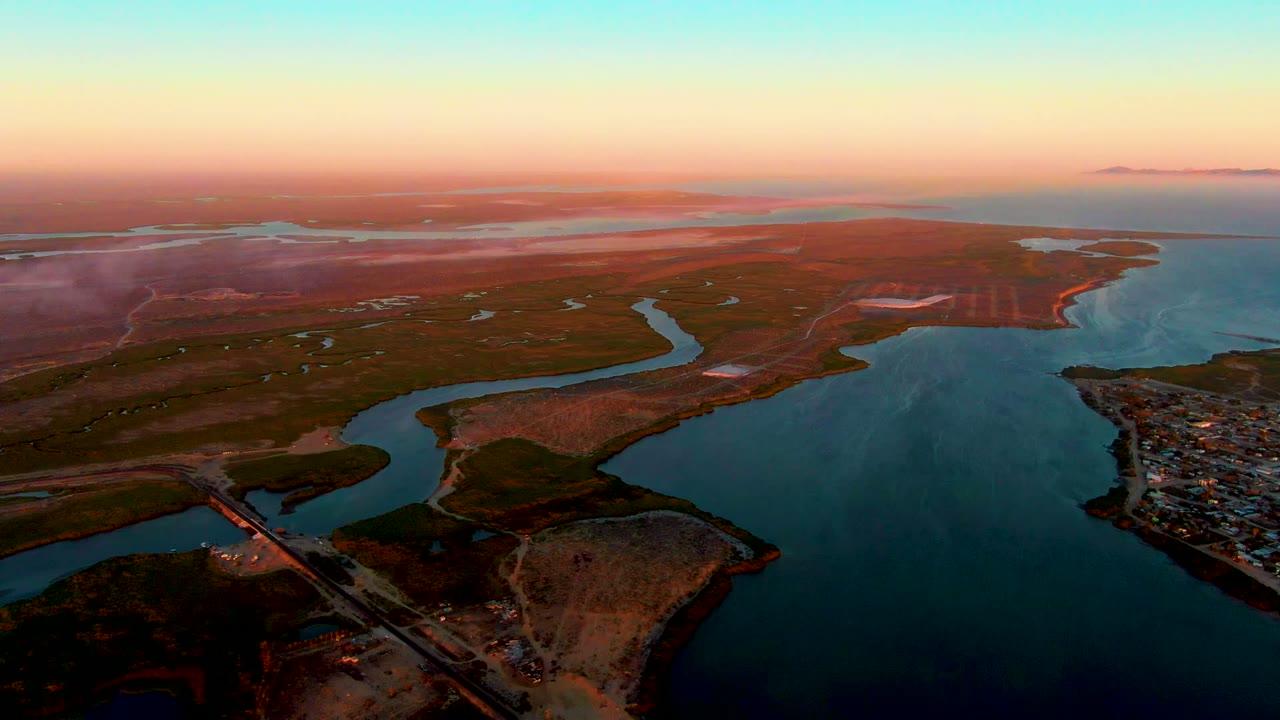 Aerial view of winding river channels beside a bridge and coastal settlement at dusk.