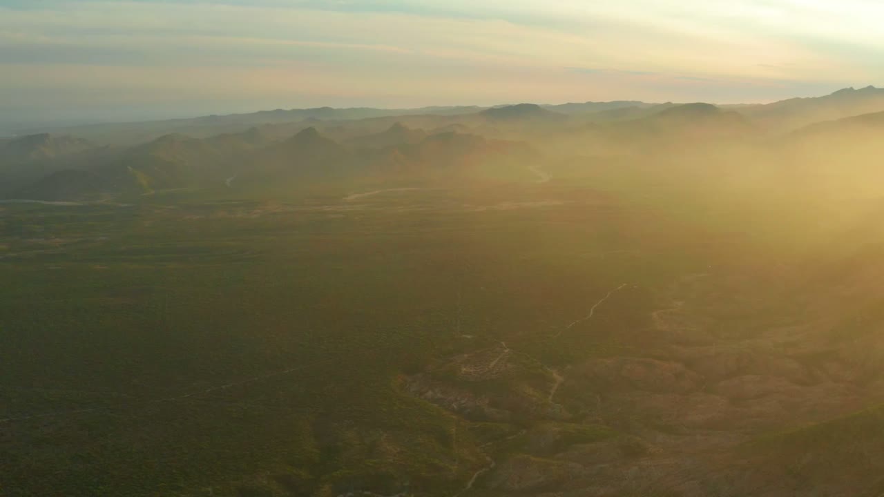 Elevated Cabo Pulmo landscape view with layered mountains in the distance, muted green ground below, golden haze at right, and no visible people.