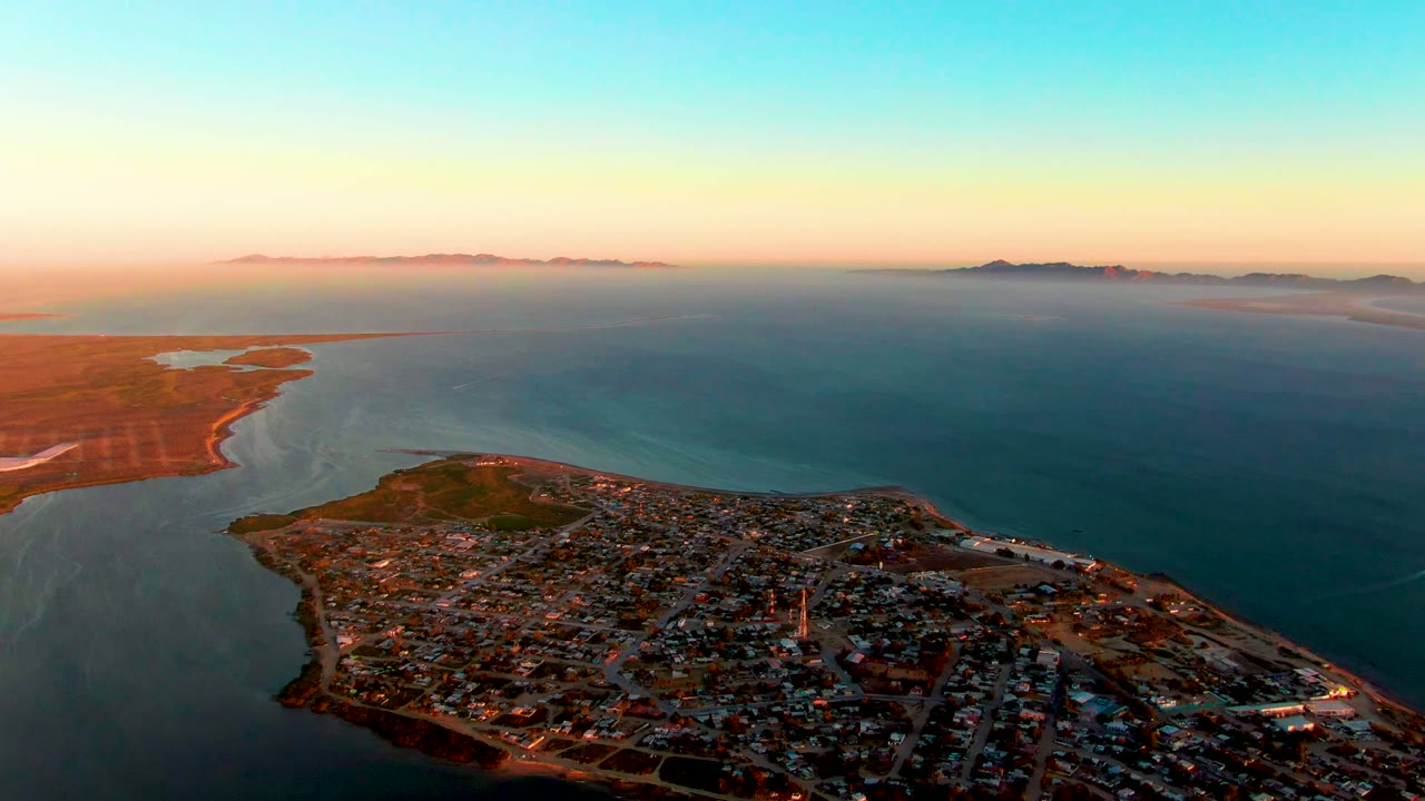 High aerial view over town rooftops, shoreline, and open water.