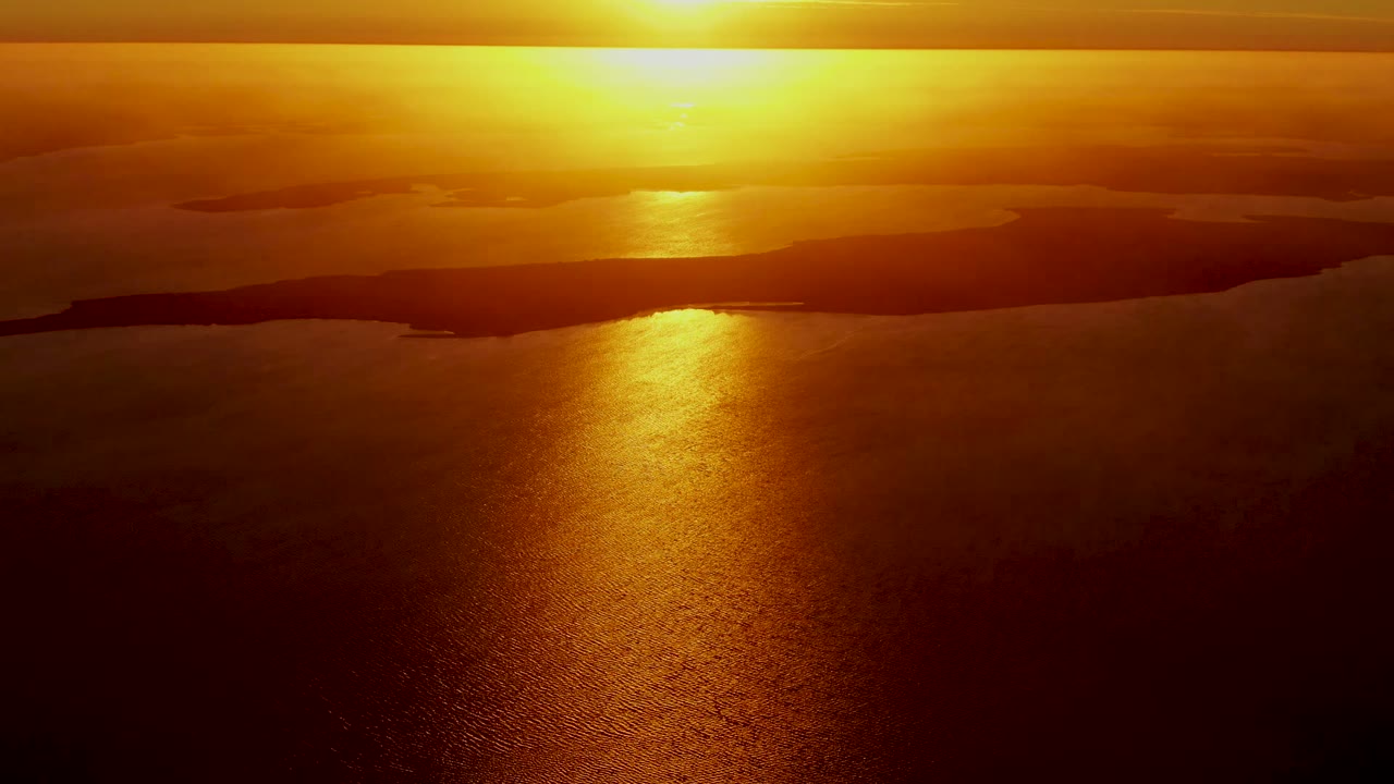 Opening frame of a San Carlos, Baja California Sur sunset with the sun low above dark landforms and a gold reflection stretching over rippled ocean water, with no visible people.