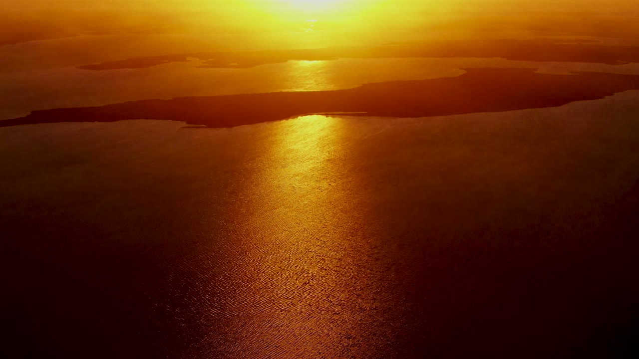 Third frame holds on the San Carlos ocean sunset, with the brightest reflection centered on the water and dark coastal silhouettes separating sea from sky, with no visible people.