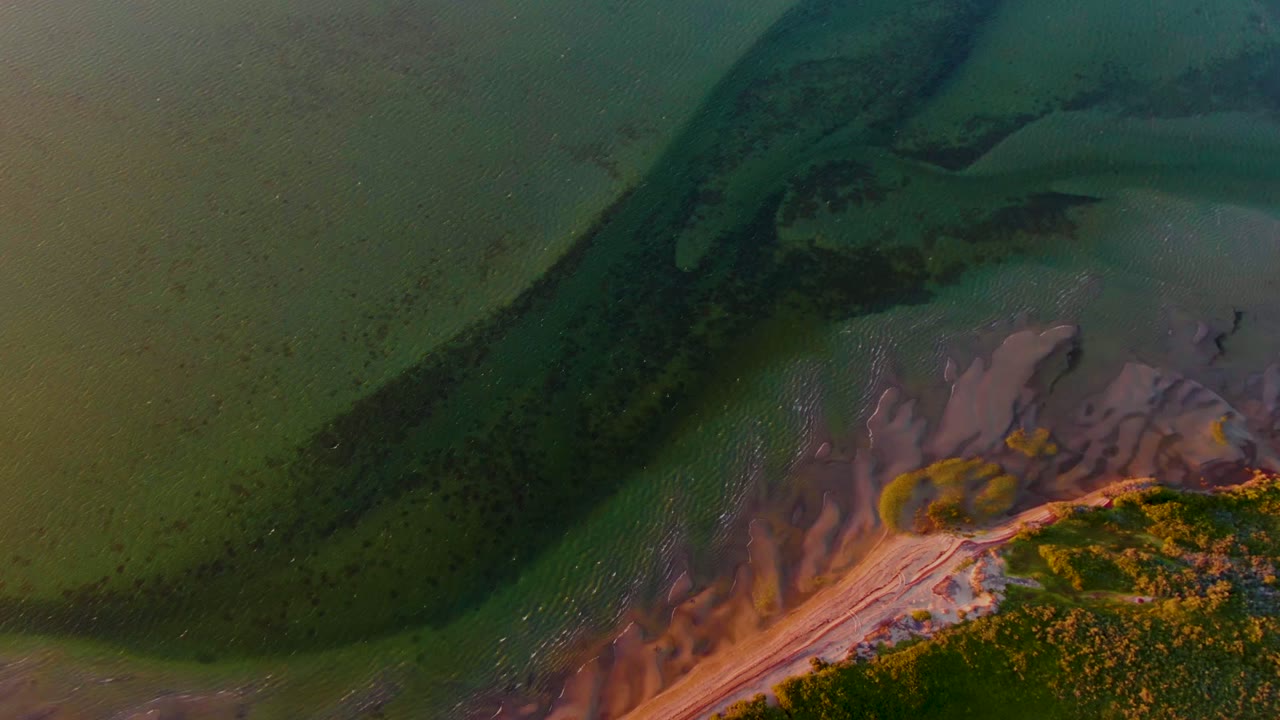 Overhead tidal shallows with dark water channel and exposed muddy beach edge.