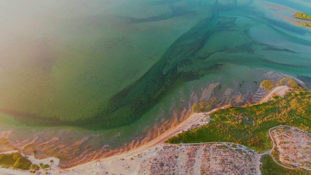 Aerial coastal tidal flat with dark water channel and sandy shoreline.