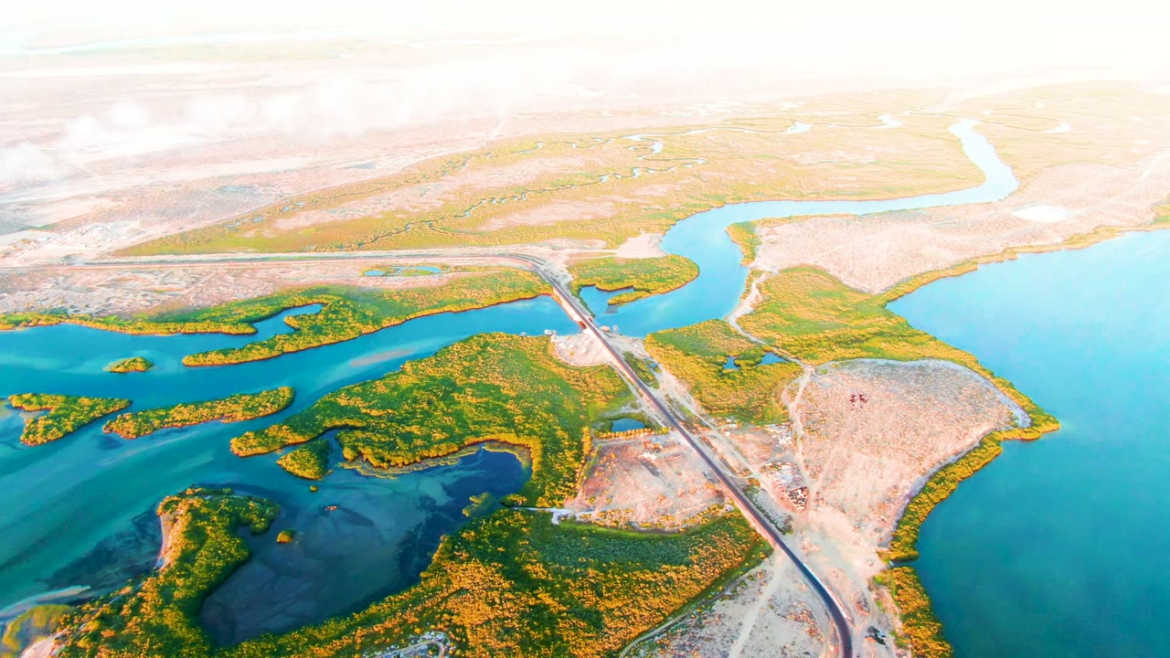 Second frame of the San Carlos aerial holds on the road bridge, branching turquoise water, dense green island patches, dry shoreline, and no visible people.