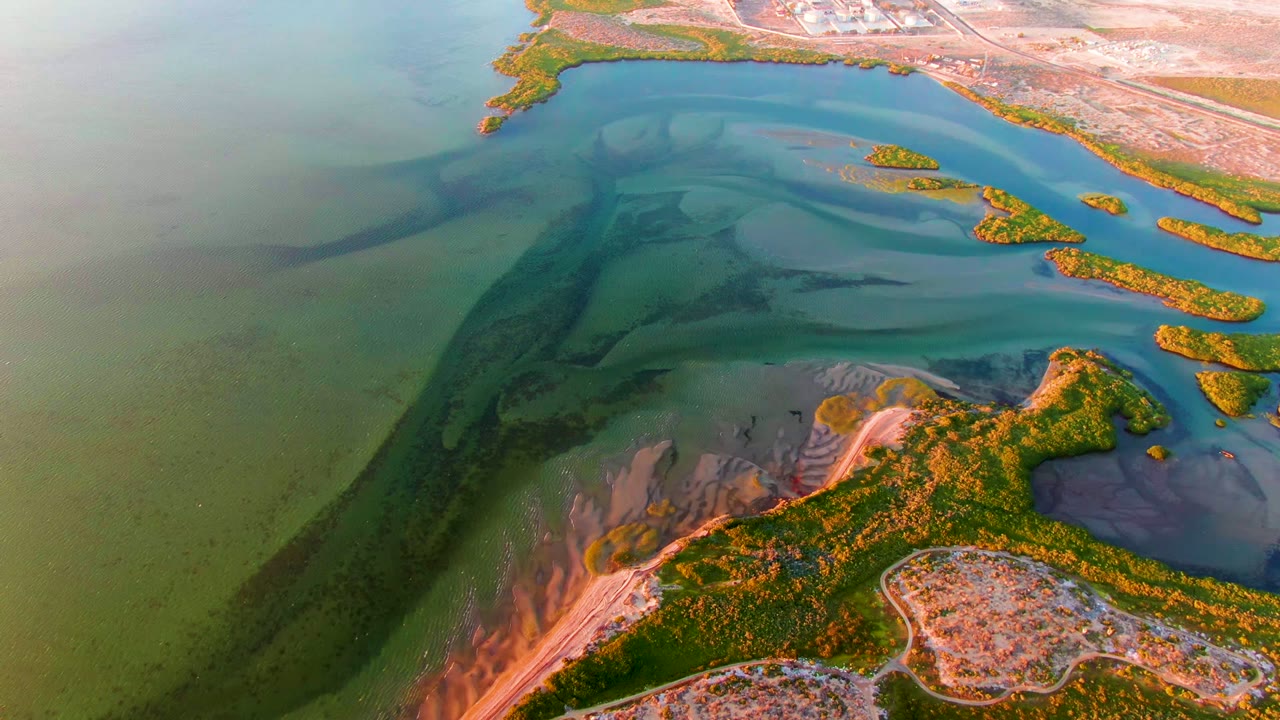 Aerial view over San Carlos, Baja California Sur showing green shallow water, a dark current channel, orange-lit mangrove shoreline, small islands, and no visible people.