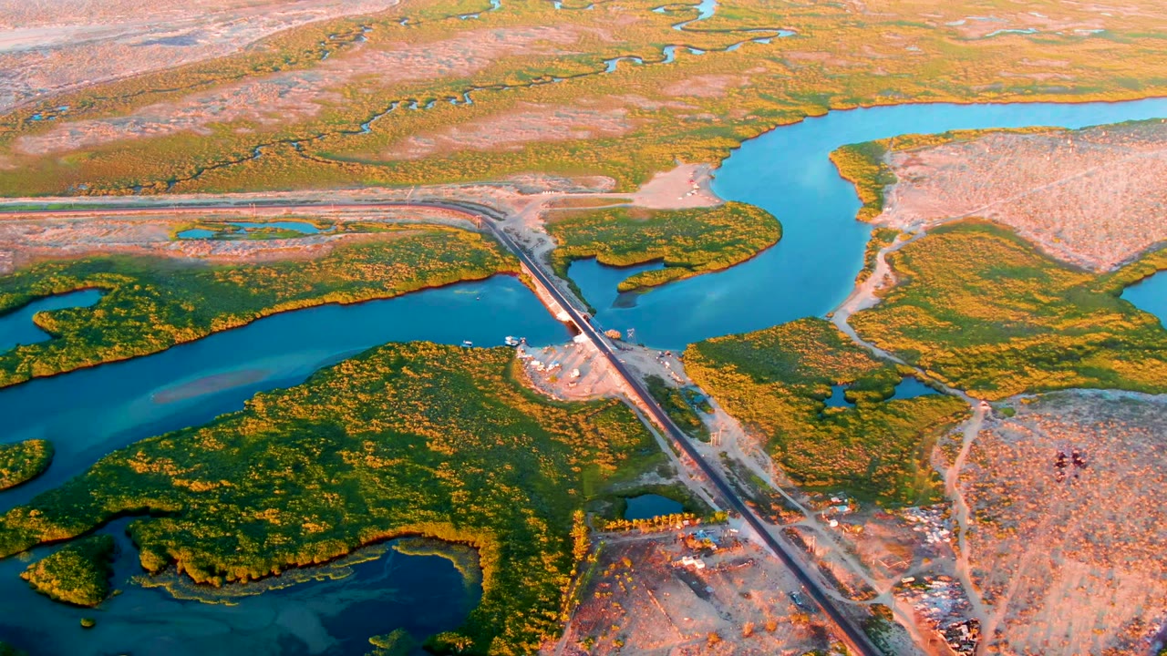 San Carlos, Baja California Sur aerial frame showing blue river channels around green wetland landforms, a straight crossing at right, pale dry terrain beyond, and no visible people.