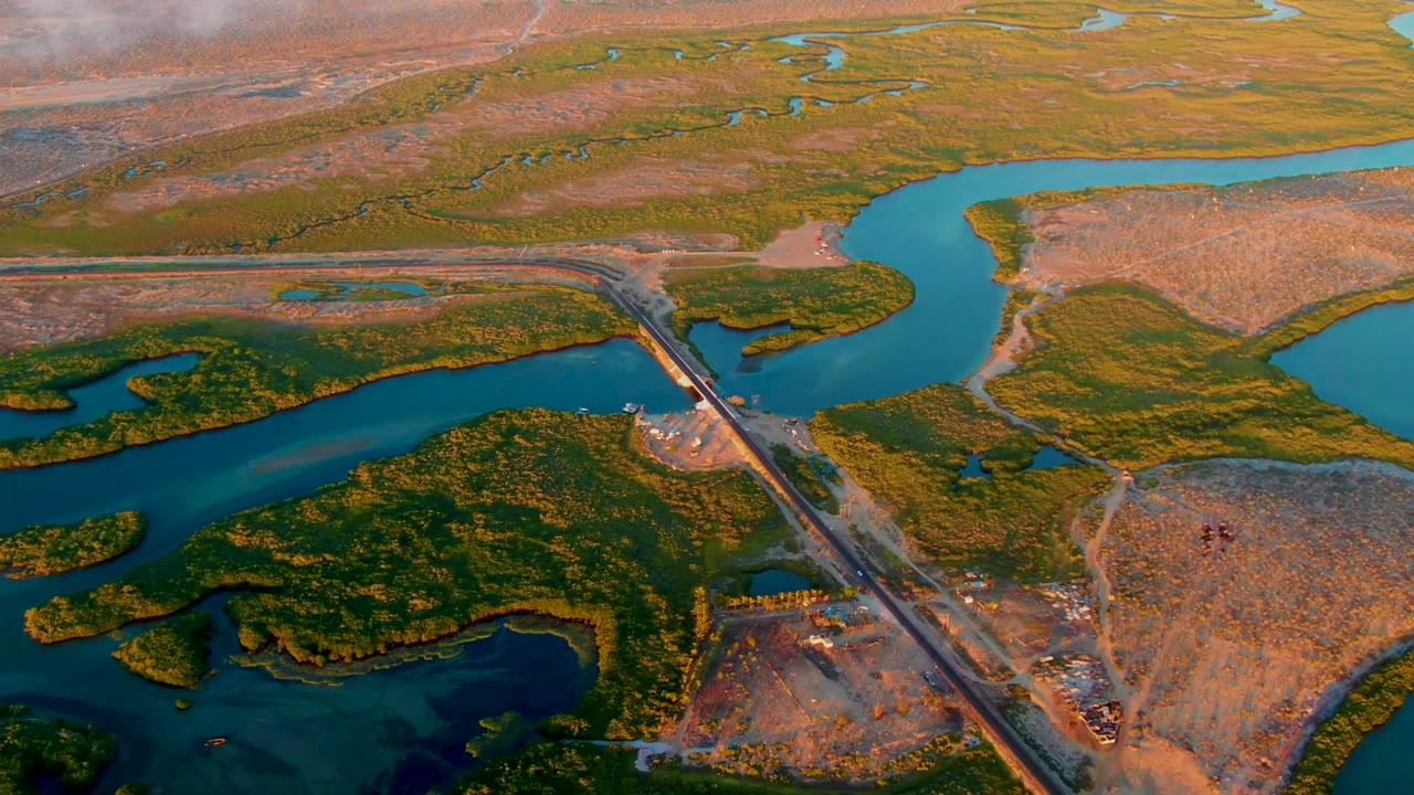 Aerial frame over San Carlos, Baja California Sur, showing a diagonal runway crossing blue-green river channels, brown flats, green marsh vegetation, and no visible people.