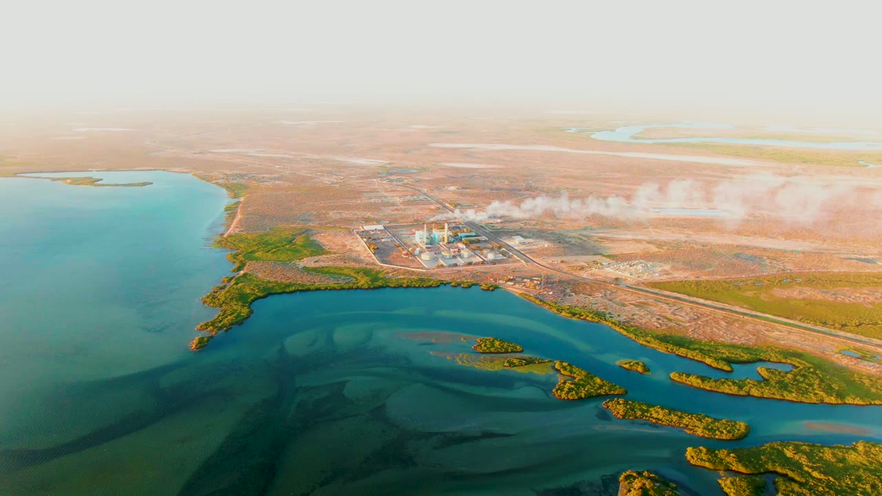 Wide drone view of a coastal industrial plant and smoke plume.
