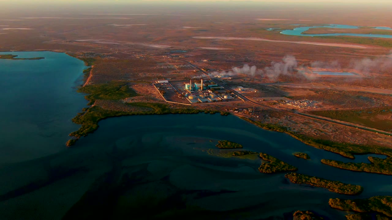 Aerial frame from San Carlos, Baja California Sur showing a power plant on a water-adjacent peninsula, dry brown land beyond it, and no visible people.