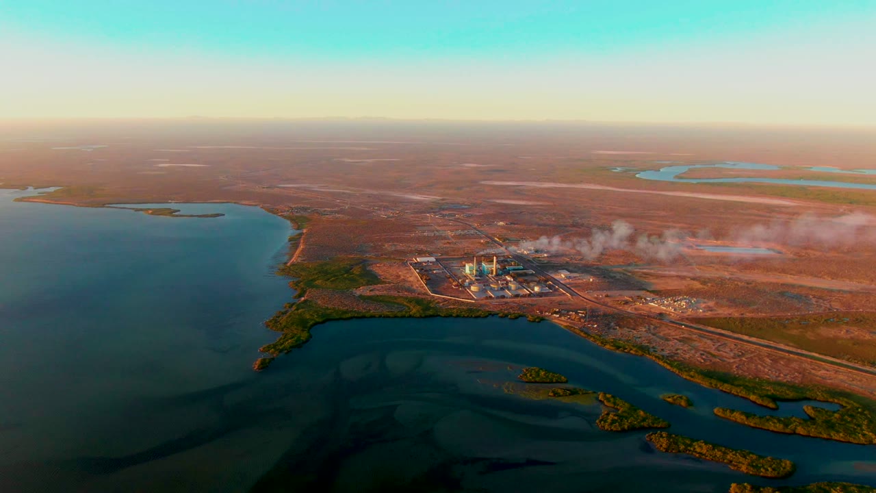 Drone view of smoke drifting from an industrial complex near a broad waterway.