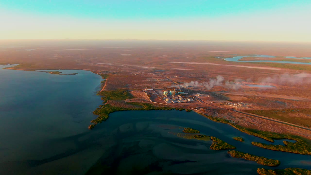 At two seconds, the frame keeps the San Carlos factory site right of center, with dark water in the foreground, scattered distant lakes, flat brown ground, and no visible people.