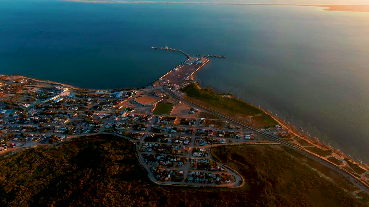 Drone view of shoreline roads, town blocks, harbor pier, and open ocean.