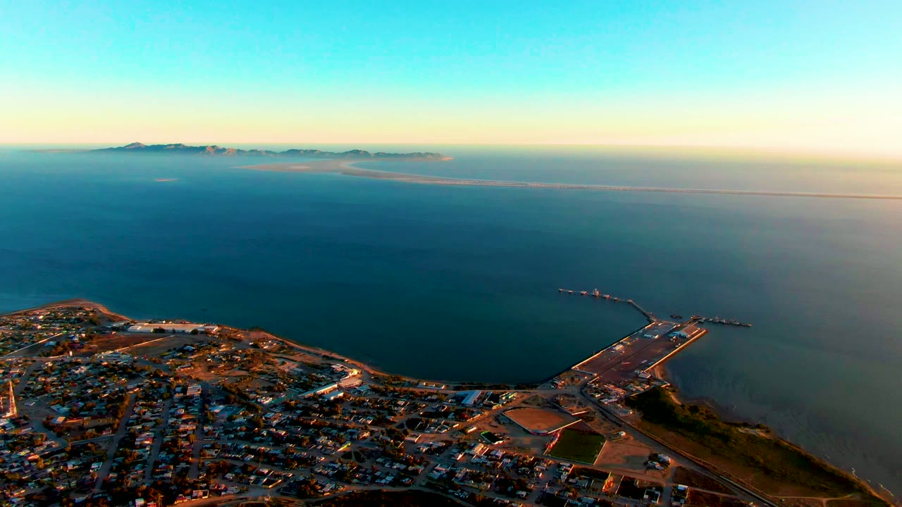 Wide aerial over shoreline town with pier extending into calm blue water