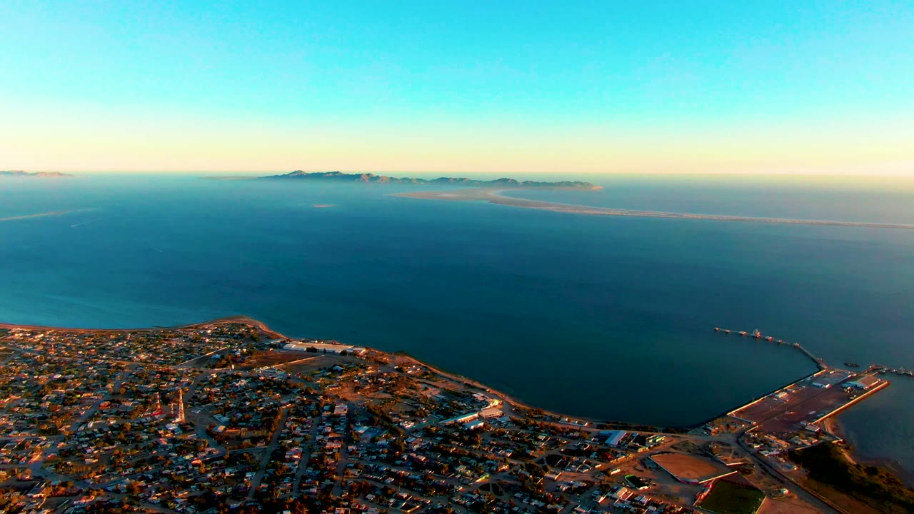 Elevated coastal view with town foreground, harbor structure, and blue ocean.