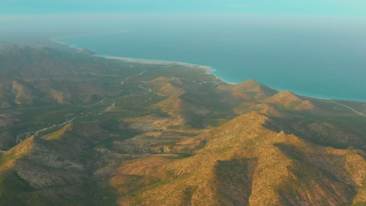 Aerial coastal mountain range with ridges, valleys, road, and ocean background.