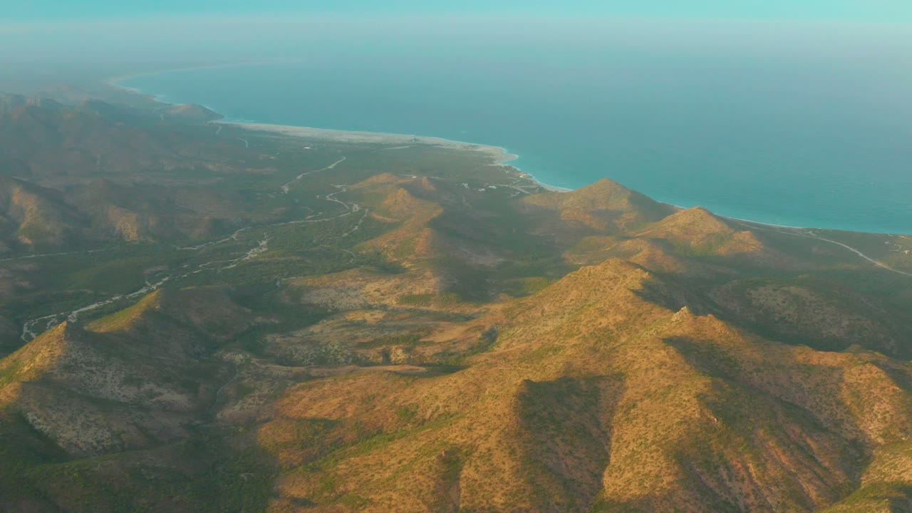 High aerial view of rugged hills descending toward a turquoise ocean coastline.
