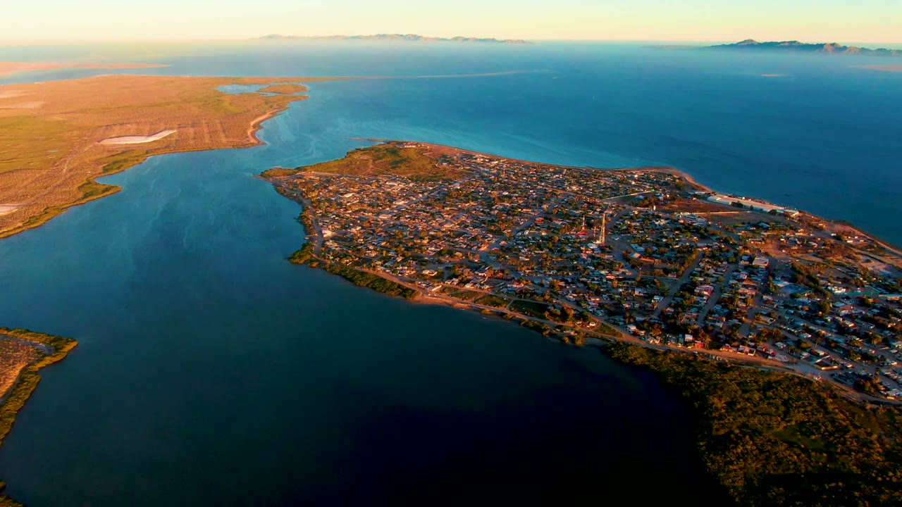Drone-height view of town blocks and roads beside calm coastal water.