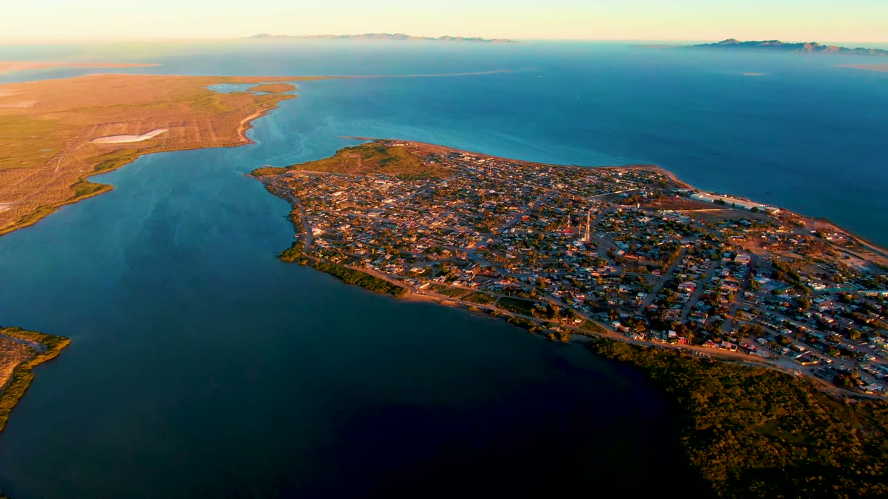 Third frame shows San Carlos from above with warm light across rooftops and roads, pale ripples near the left inlet, open water stretching to the horizon, and no visible people.