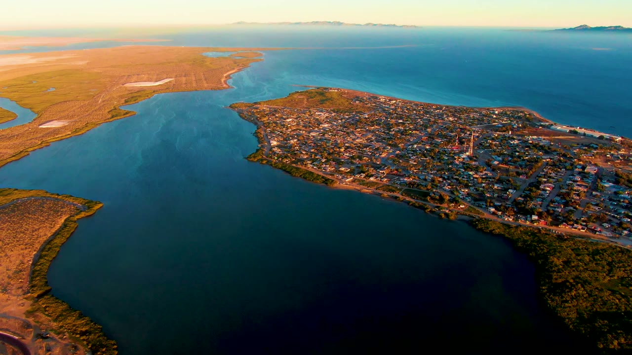 Wide drone view of shoreline, town buildings, and dark bay water.