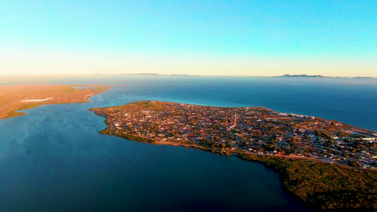 Coastal town on a peninsula with blue water and dry land beyond.